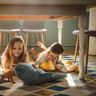 Illustration - Ihr Experte für schönes Wohnen - Kinder spielen unter dem Küchentisch auf einem gemütlichen Teppich.
